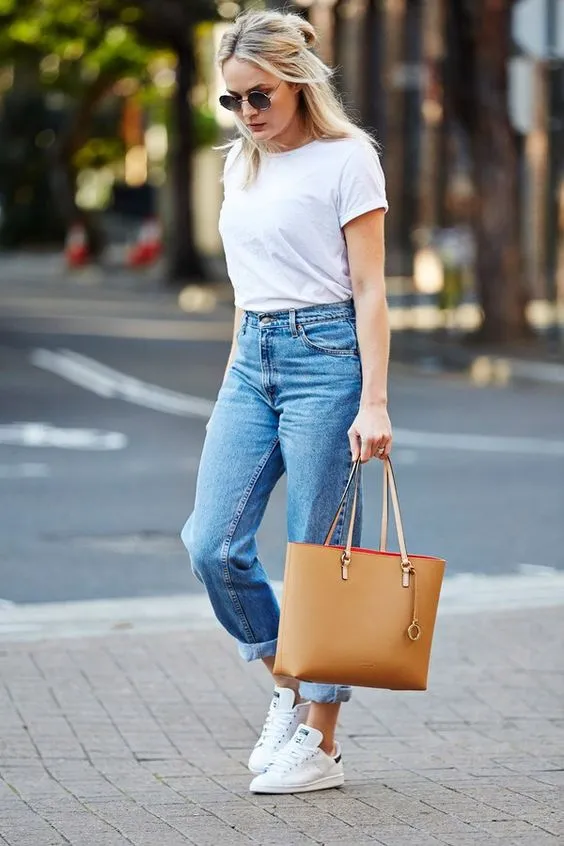 Повседневный образ - прямые светлые джинсы, простая белая футболка и кроссовки. Образ дополнен очками и коричневой сумкой.