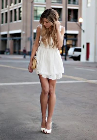 Девушка в коротком белом платье с маленькой сумочкой