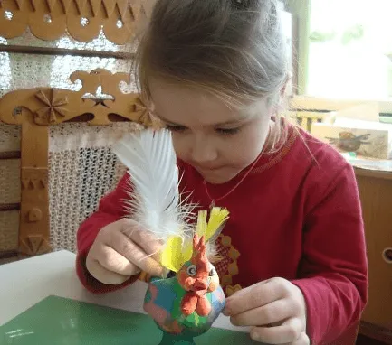 Девочка украшает птицу пером