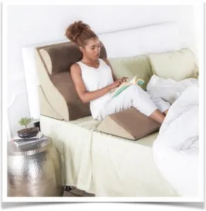 Девушка читает книгу на кровати с подушкой под спиной и ногами